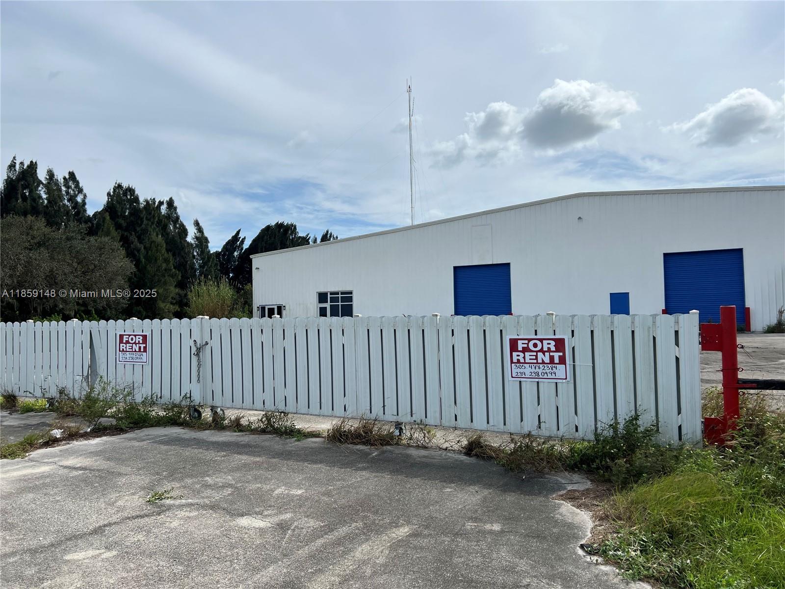 A white warehouse building sits behind a white picket fence with for rent signs — 14961 SR W78, Moore Haven FL 33471, MOORE HAVEN, FL