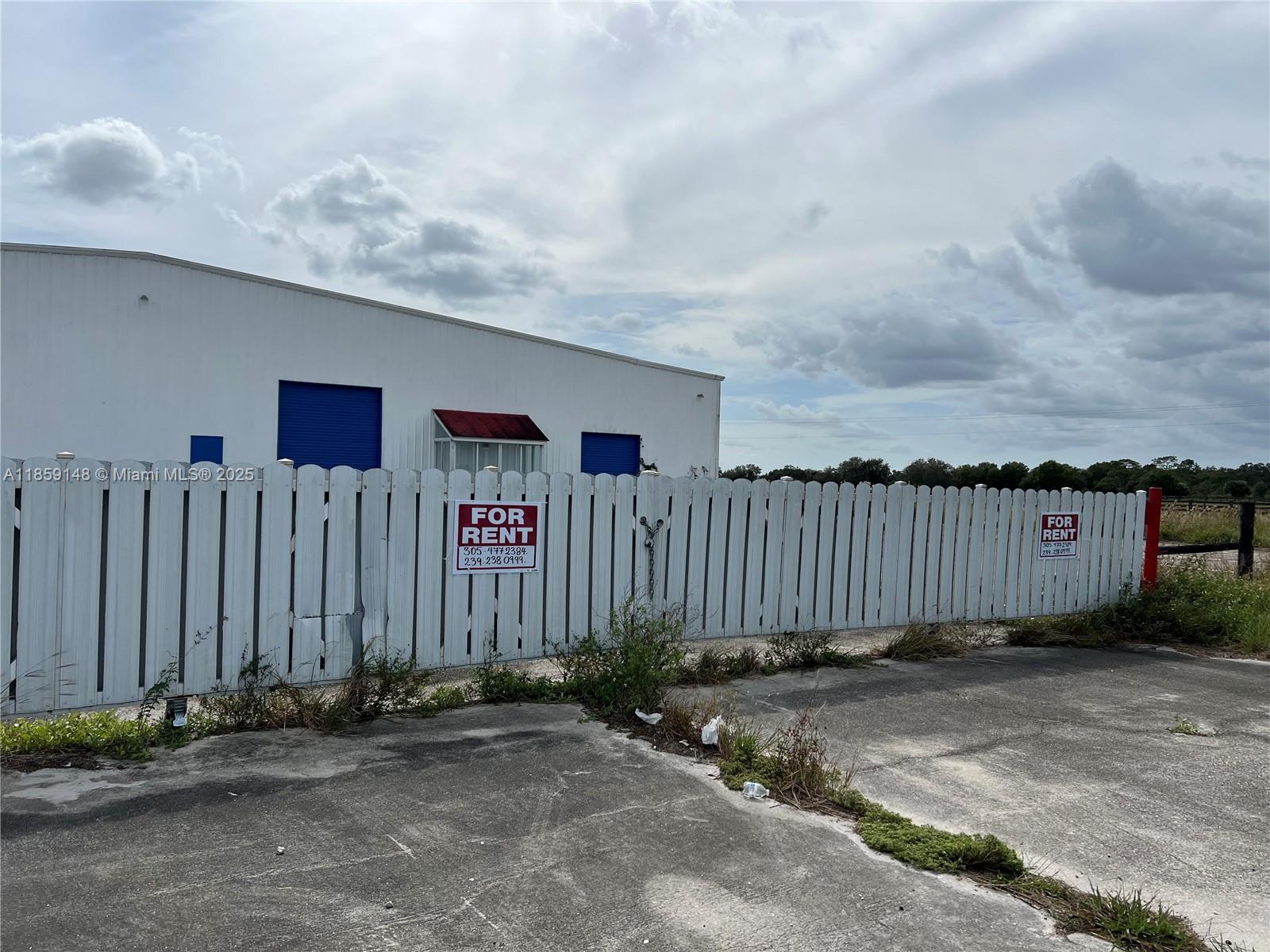 A white warehouse building sits behind a white picket fence with two for rent signs — 14961 SR W78, Moore Haven FL 33471, MOORE HAVEN, FL