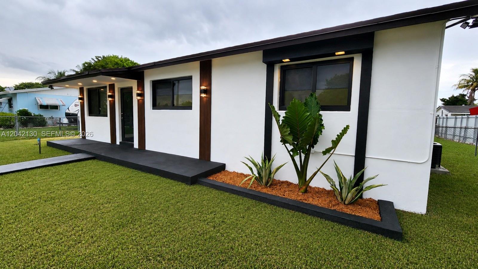 A modern white house exterior features black window frames, wood-slat accents, and a black porch — 19721 SW 114th Pl, Miami FL 33157, MIAMI, FL