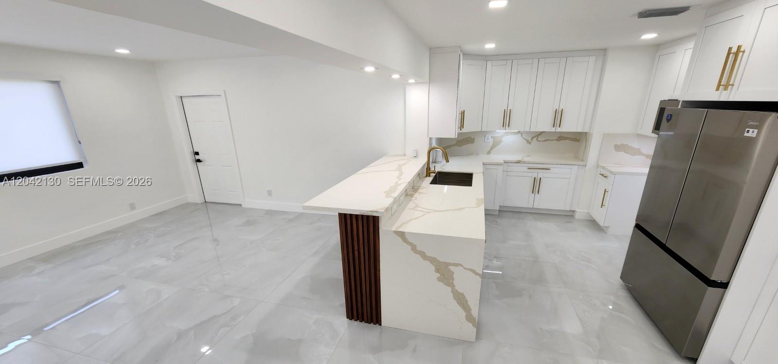A modern kitchen features white cabinetry, marble-patterned countertops, a tiered island, and light-colored tile flooring — 19721 SW 114th Pl, Miami FL 33157, MIAMI, FL