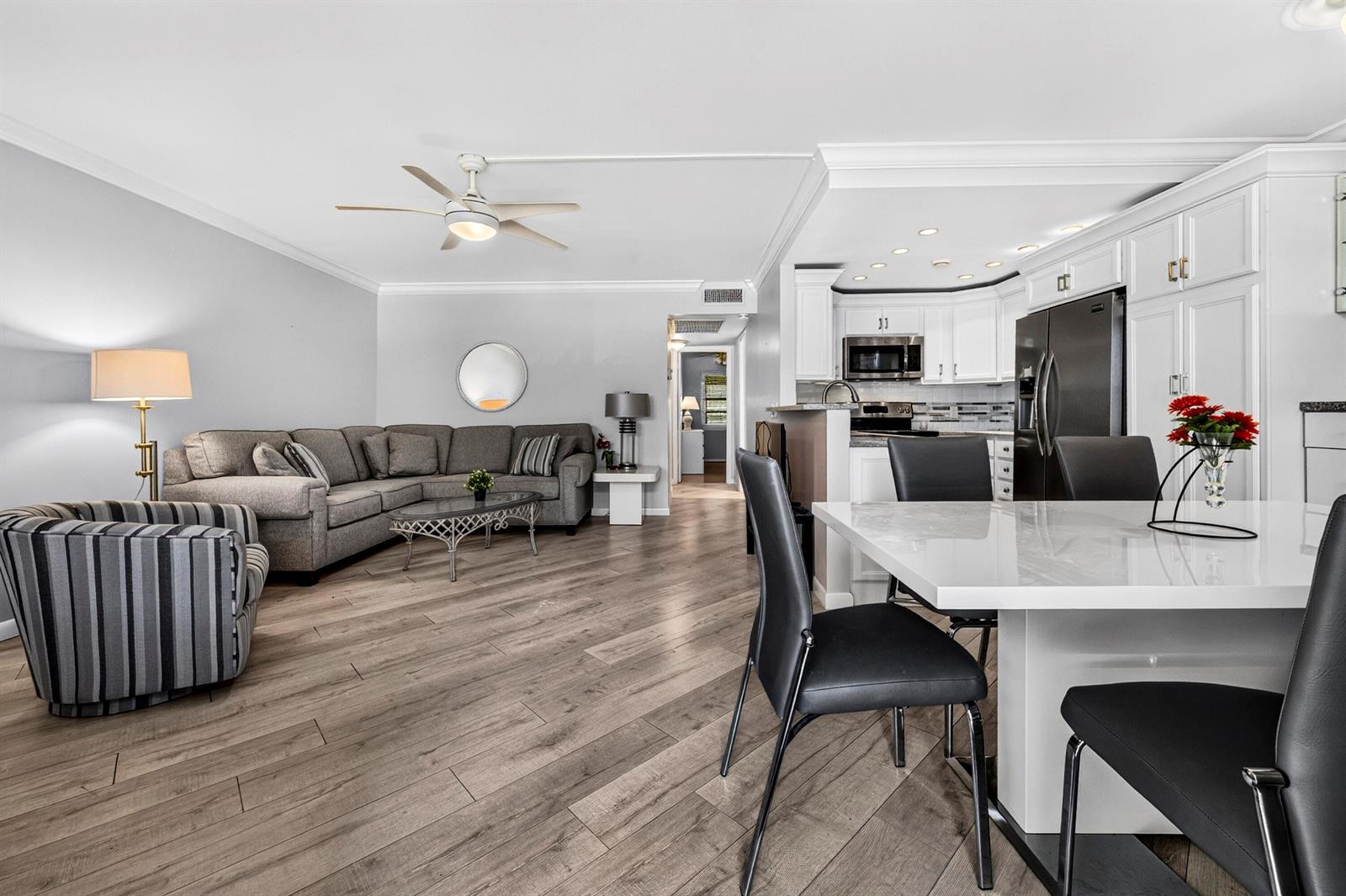 An open-concept living and dining area features wood-look flooring, a sectional sofa, and white cabinetry — 1039 Berkshire B # 1039, Deerfield Beach FL 33442, DEERFIELD BEACH, FL