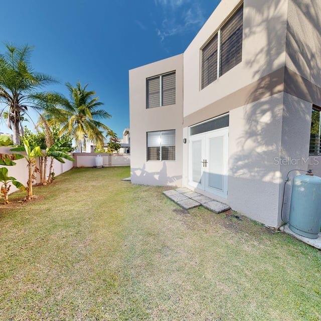 A grassy backyard features a two-story beige house with double glass doors and propane tanks — ENCANTADA NW PACIFICA, TRUJILLO ALTO, PR