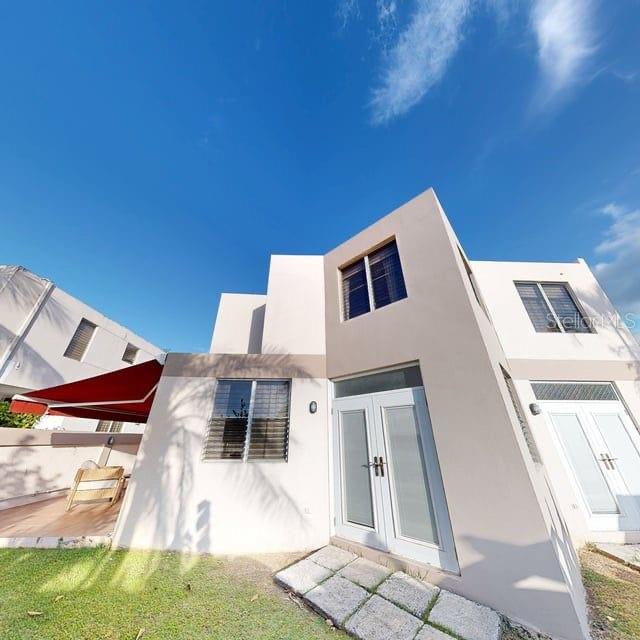 A low-angle exterior view of a modern two-story house with a red awning and patio — ENCANTADA NW PACIFICA, TRUJILLO ALTO, PR