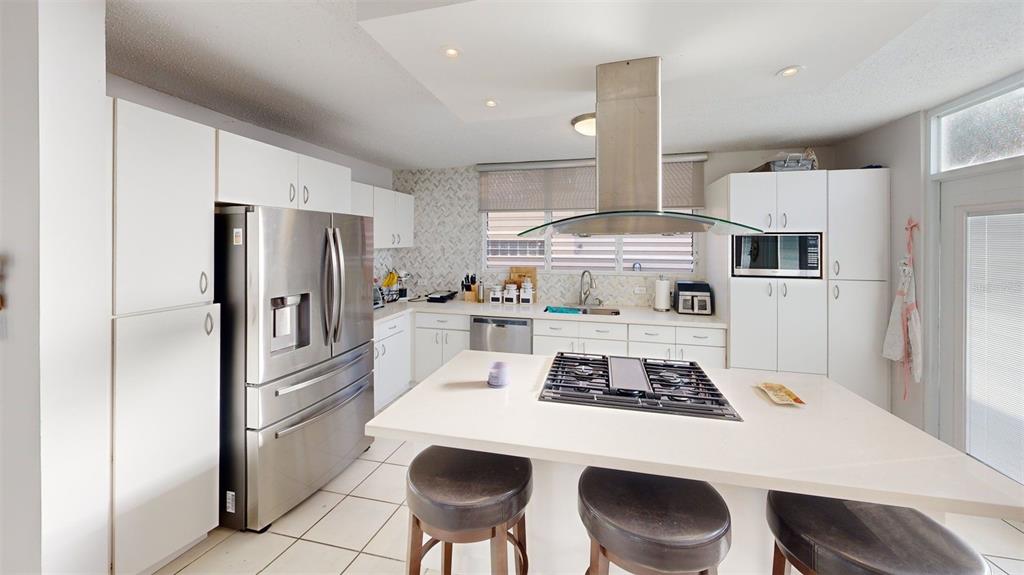 A modern kitchen features white cabinetry, stainless steel appliances, a center island, and tile flooring — ENCANTADA NW PACIFICA, TRUJILLO ALTO, PR