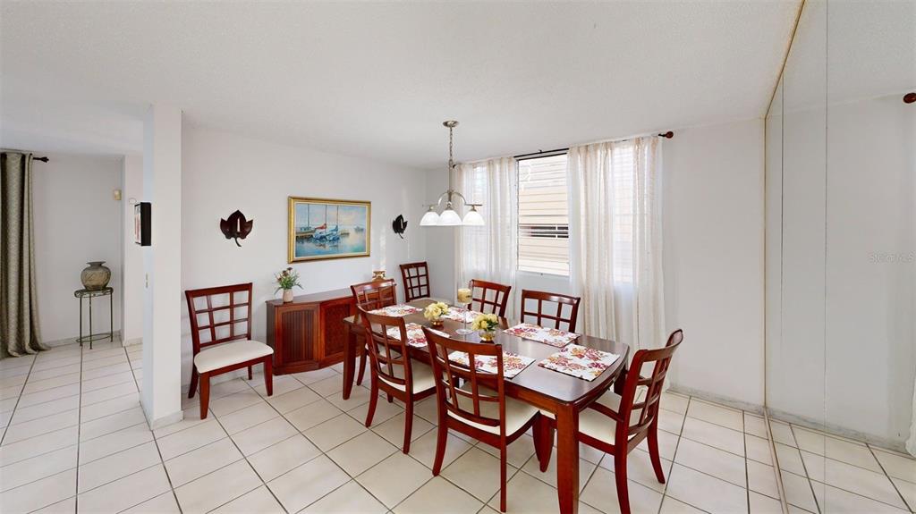 A dining room features a wooden table with six chairs, tiled floors, and a chandelier — ENCANTADA NW PACIFICA, TRUJILLO ALTO, PR