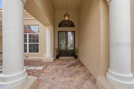 A covered entryway features a brick paver floor, two large white columns, and double front doors — 18655 AVENUE CAPRI, LUTZ, FL