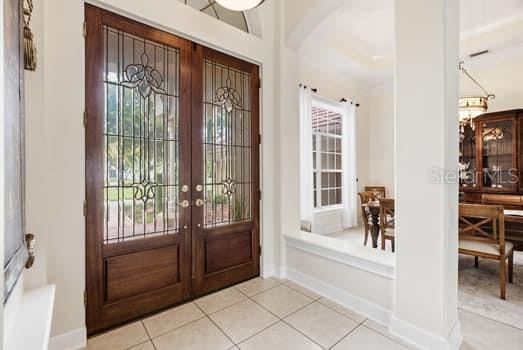 An entryway with double wood and glass doors, tile flooring, and an adjacent dining area — 18655 AVENUE CAPRI, LUTZ, FL