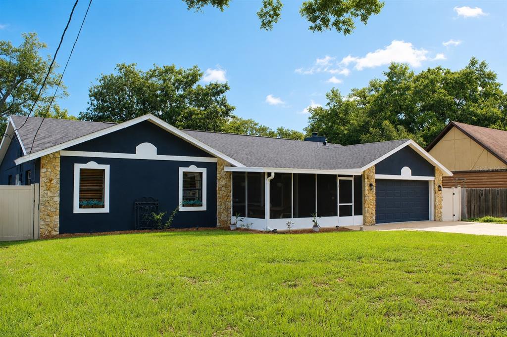 A single-story house with dark blue siding, stone accents, a screened porch, and a garage — 27627 LOIS DRIVE, TAVARES, FL