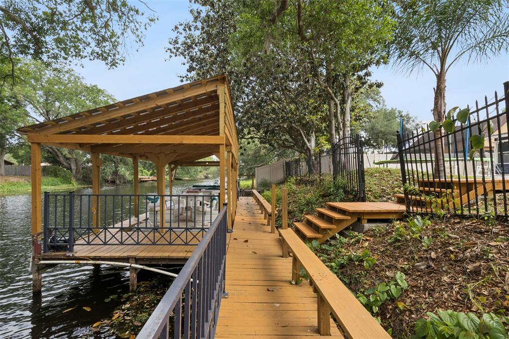 A wooden dock with a covered boat slip sits along a canal next to stairs — 27627 LOIS DRIVE, TAVARES, FL