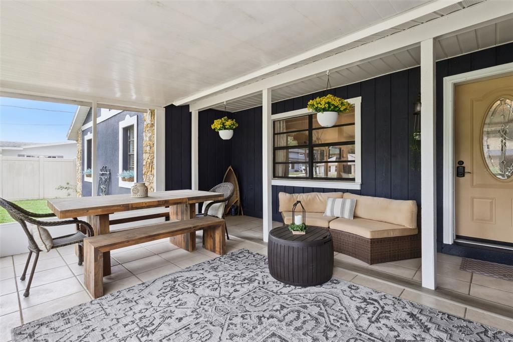 A covered patio features a wooden dining set, wicker seating, and dark blue exterior siding — 27627 LOIS DRIVE, TAVARES, FL