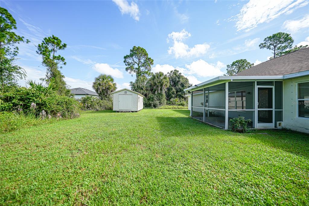 A grassy backyard features a small storage shed and a screened-in patio attached to a house — 1471 PRAIRIE TERRACE, NORTH PORT, FL