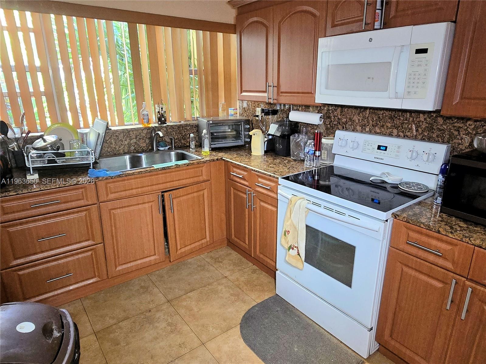 A kitchen features wood cabinets, granite countertops, a white stove, and a double sink — 940 NE 199th St # 114, Miami FL 33179, MIAMI, FL