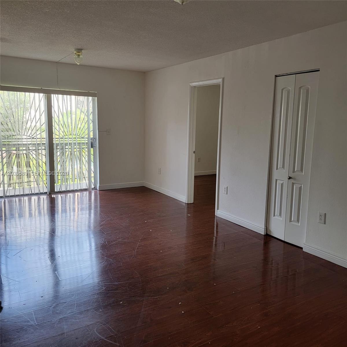 An empty room features dark wood flooring, white walls, a sliding glass door, and a closet — 4841 NW 7th St # 4, Miami FL 33126, MIAMI, FL