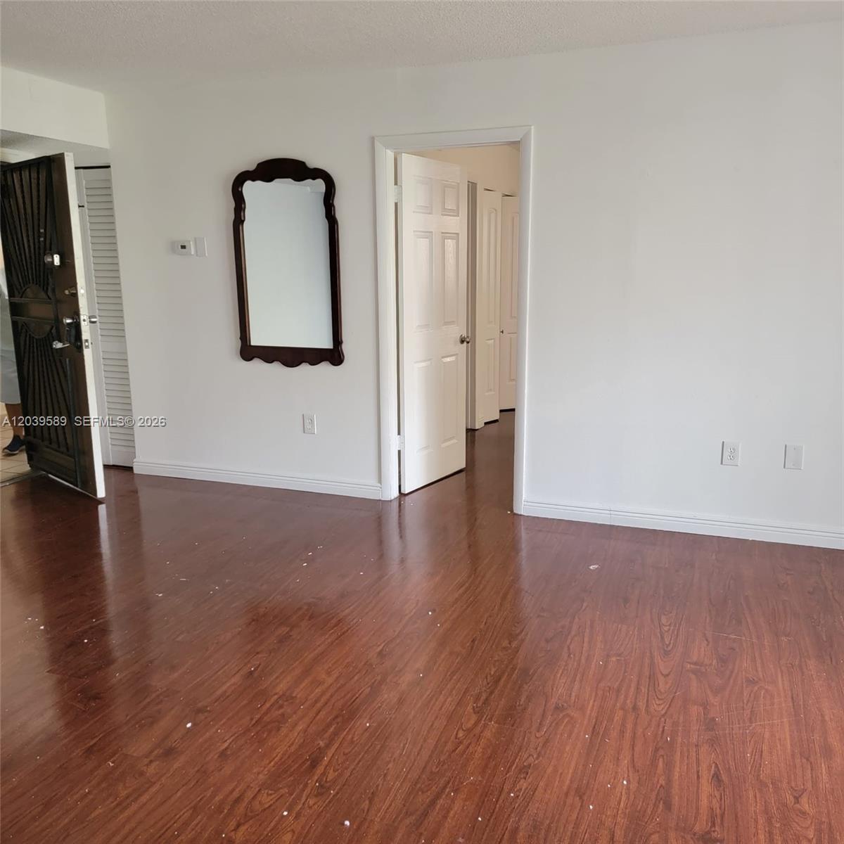 An empty room features dark wood-look flooring, white walls, and a dark-framed wall mirror — 4841 NW 7th St # 4, Miami FL 33126, MIAMI, FL