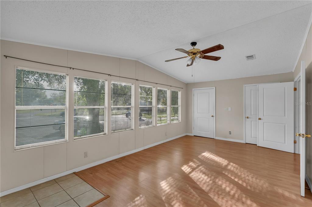 A room with wood-look flooring, a ceiling fan, multiple windows, and two white doors — 202 DANA COURT, KISSIMMEE, FL