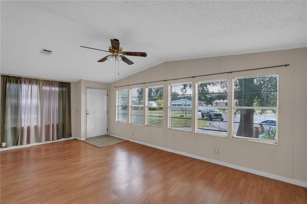 A living room features wood-look flooring, a ceiling fan, and large windows with blinds — 202 DANA COURT, KISSIMMEE, FL