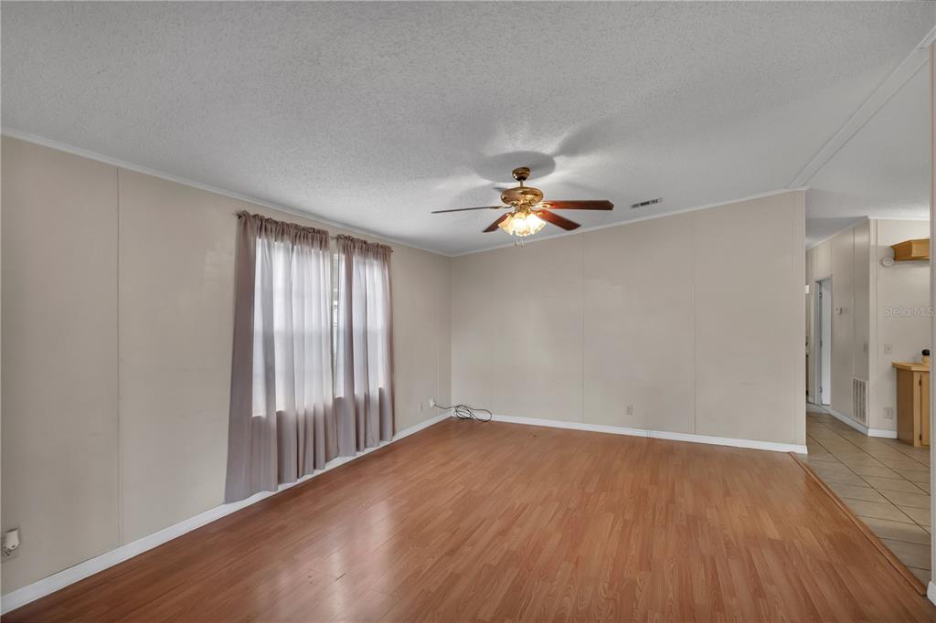 An empty living room features light-colored walls, wood-look flooring, and a ceiling fan — 202 DANA COURT, KISSIMMEE, FL