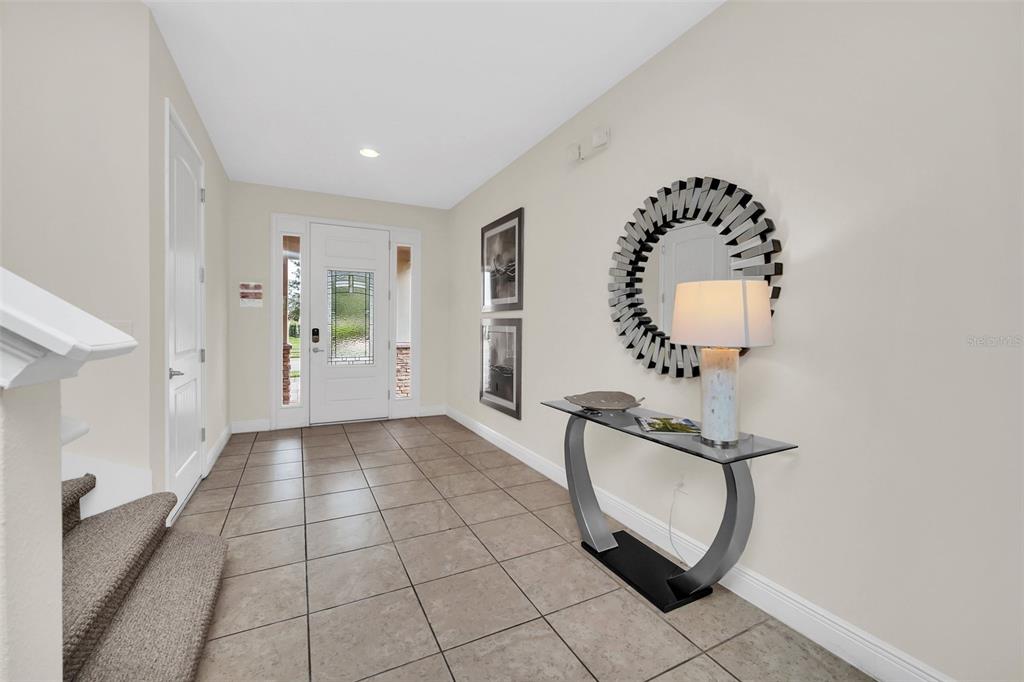 A tiled entryway features a white front door, a glass console table, and a sunburst mirror — 400 BURMA STREET, KISSIMMEE, FL