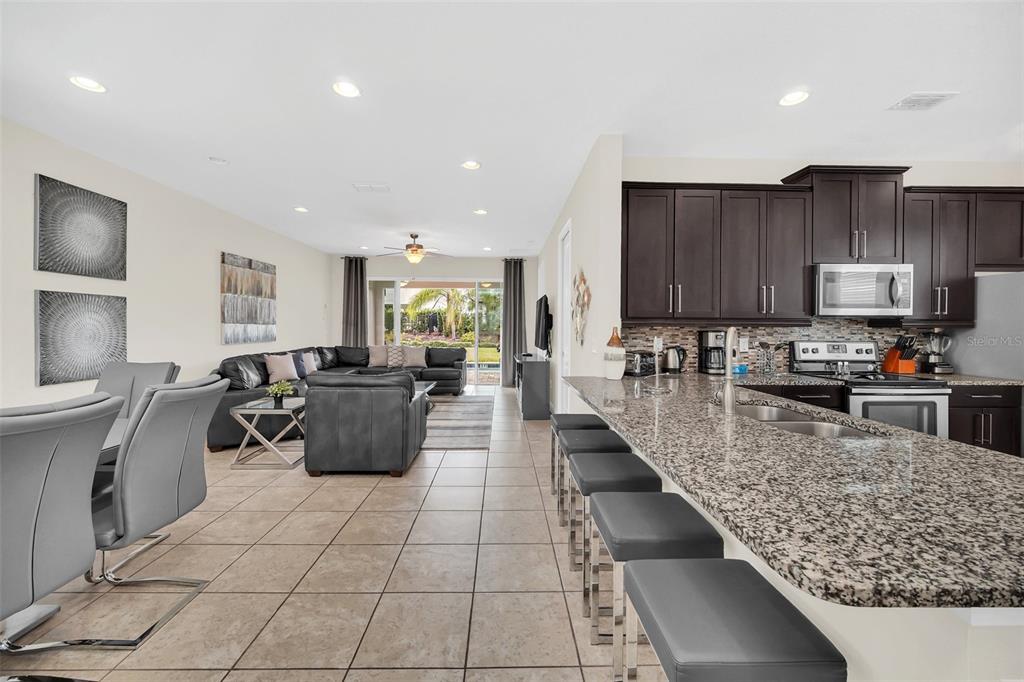 An open-concept kitchen with granite countertops overlooks a living room with tile flooring — 400 BURMA STREET, KISSIMMEE, FL