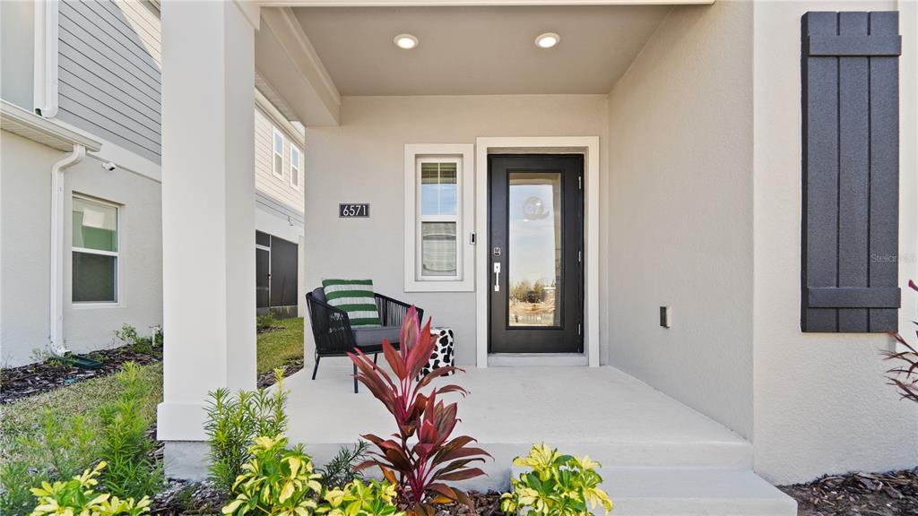 A covered concrete front porch features a black door, a chair, and landscaping — 6571 EASTWOOD CROSS DRIVE, ORLANDO, FL