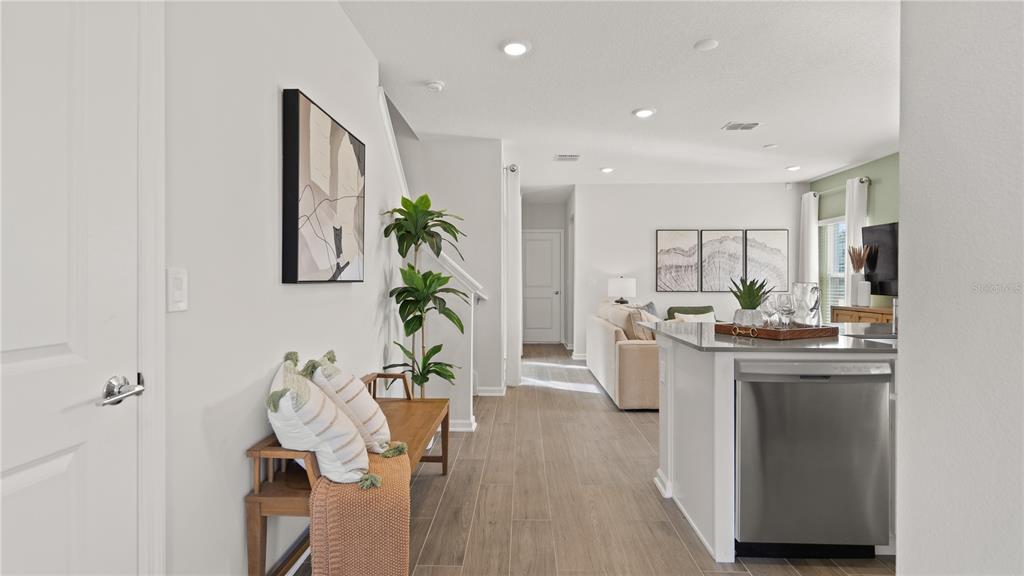 A view of a modern kitchen island, hallway, and living area with wood-look tile flooring — 6571 EASTWOOD CROSS DRIVE, ORLANDO, FL