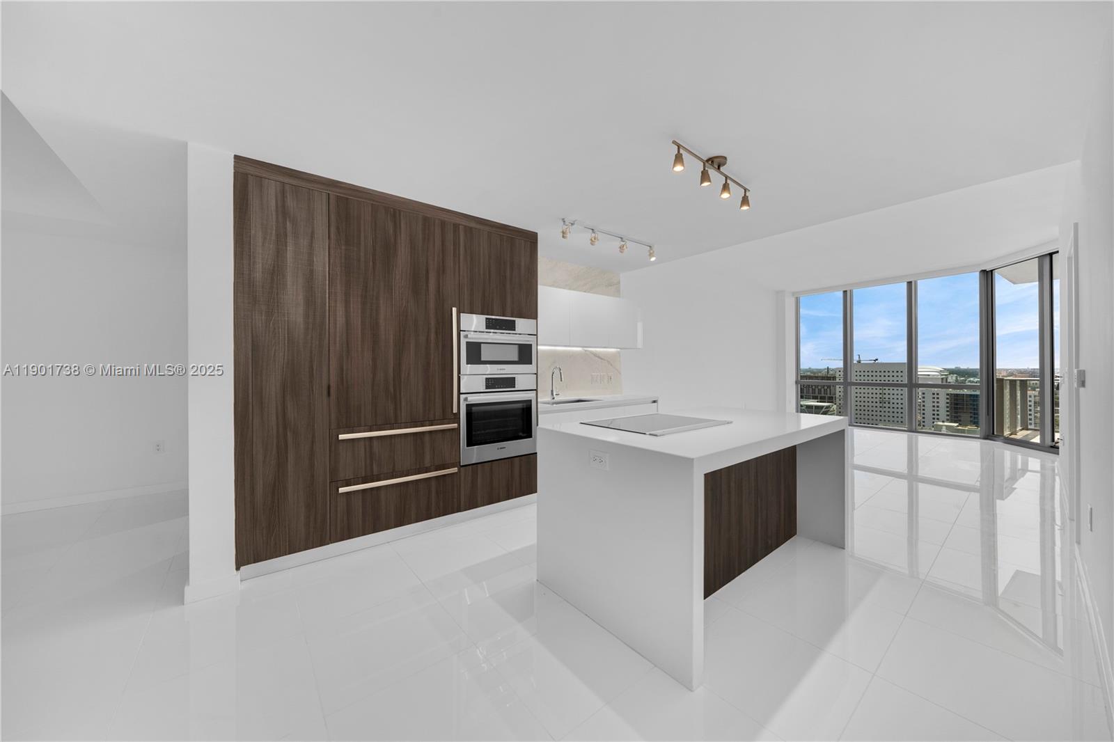 A modern kitchen features dark wood cabinetry, a white island, and floor-to-ceiling windows — 851 NE 1st AVE # 2106, Miami FL 33132, MIAMI, FL