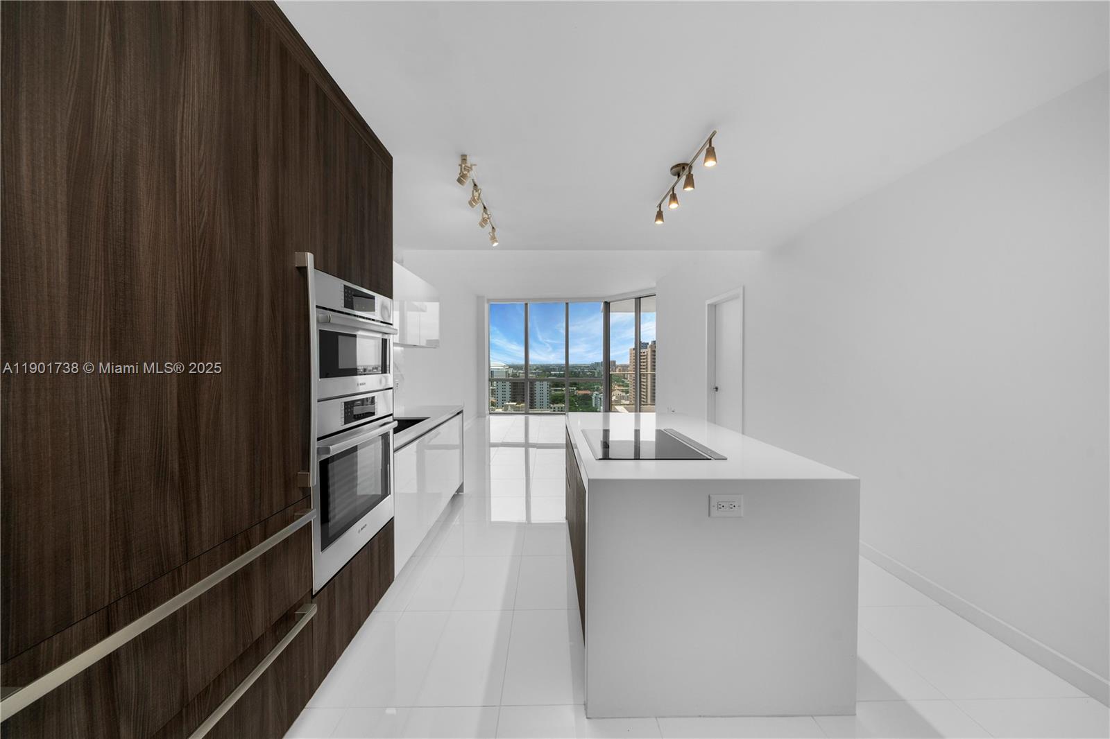A modern kitchen features dark wood cabinetry, a white island, and floor-to-ceiling windows — 851 NE 1st AVE # 2106, Miami FL 33132, MIAMI, FL