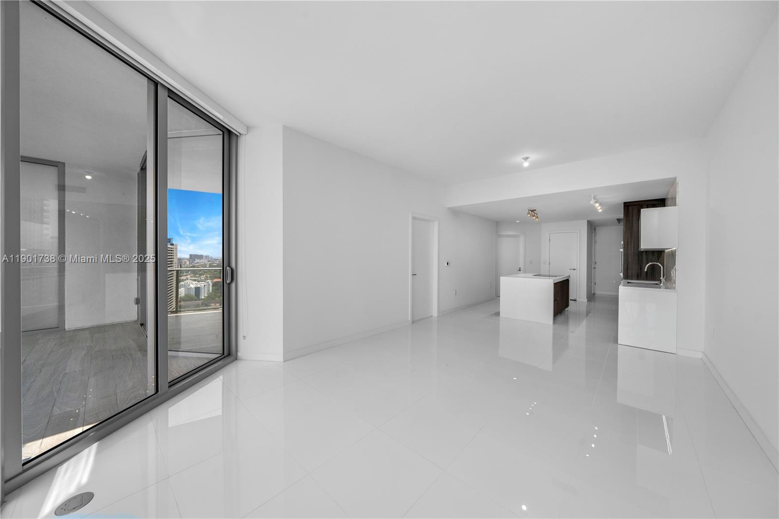 A modern, minimalist living area features white tile floors, a kitchen island, and balcony access — 851 NE 1st AVE # 2106, Miami FL 33132, MIAMI, FL