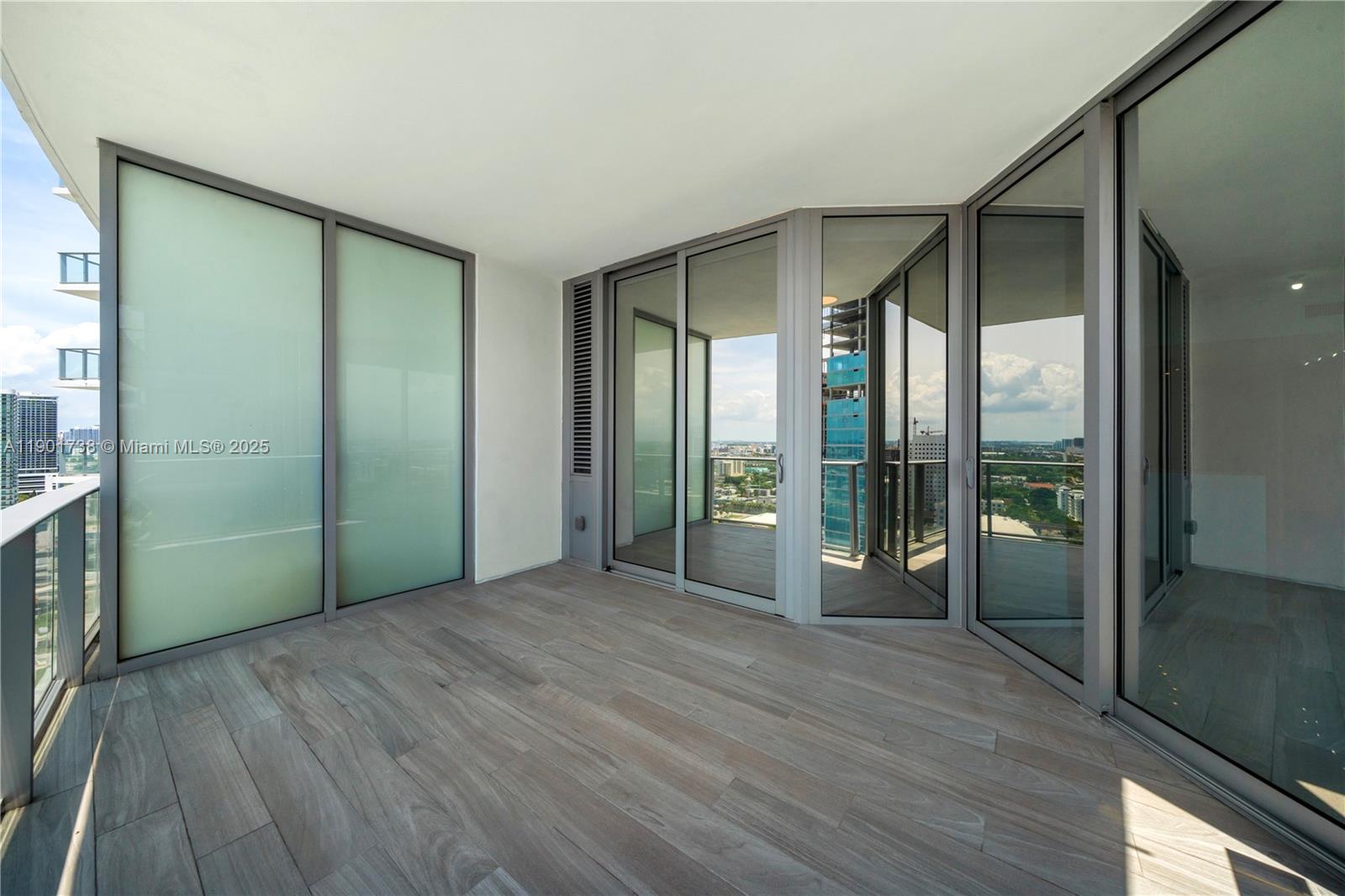 A modern balcony features wood-look tile flooring, glass railings, and floor-to-ceiling sliding glass doors — 851 NE 1st AVE # 2106, Miami FL 33132, MIAMI, FL