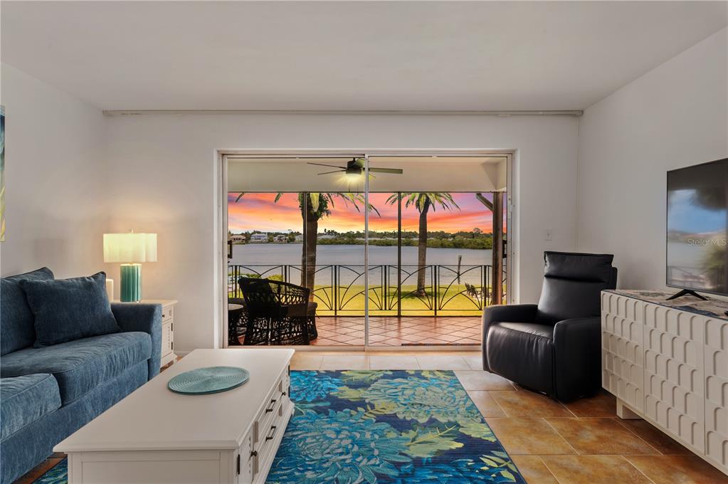 A living room features a blue sofa, a black recliner, and sliding doors overlooking a lake — 6005 MIDNIGHT PASS ROAD UNIT N13, SARASOTA, FL