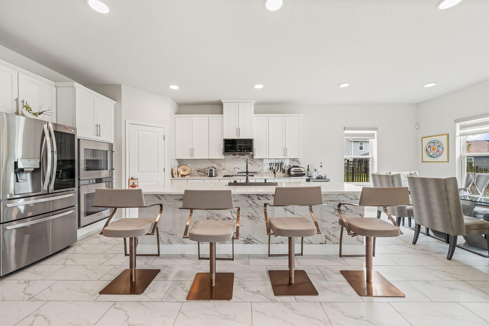 A modern kitchen features white cabinets, a marble-topped island, and four bar stools — 19227 Broad Shore Walk, Loxahatchee FL 33470, LOXAHATCHEE, FL