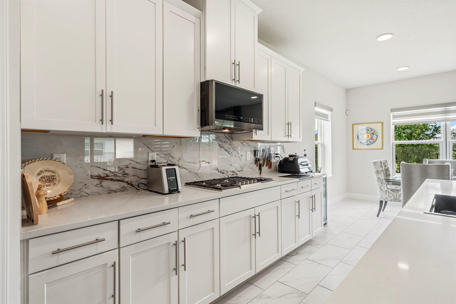 A modern white kitchen features marble-style countertops, a gas cooktop, and stainless steel appliances — 19227 Broad Shore Walk, Loxahatchee FL 33470, LOXAHATCHEE, FL