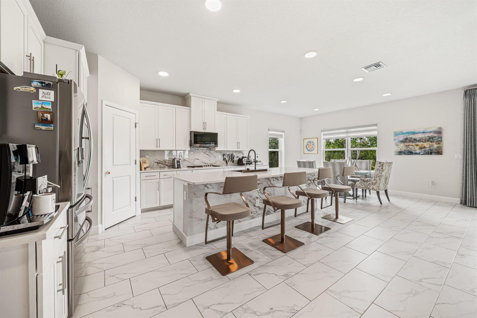 A modern kitchen features white cabinetry, a marble-topped island with bar stools, and tiled floors — 19227 Broad Shore Walk, Loxahatchee FL 33470, LOXAHATCHEE, FL