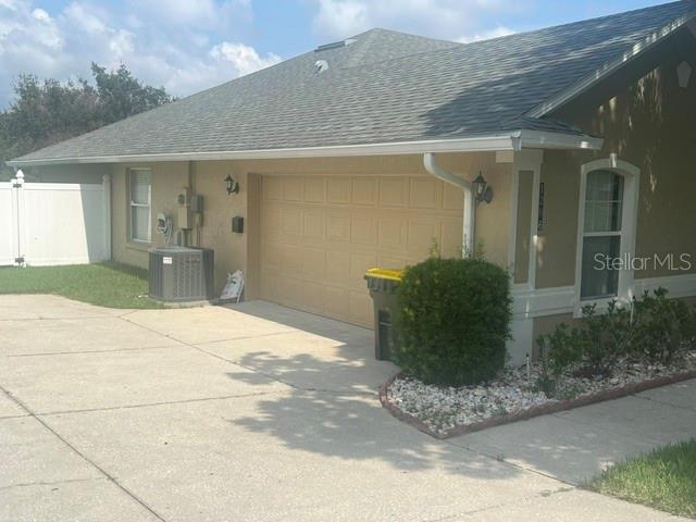 A tan house exterior features a two-car garage, a concrete driveway, and a small garden — 1206 BRENTWOOD DRIVE, CLERMONT, FL