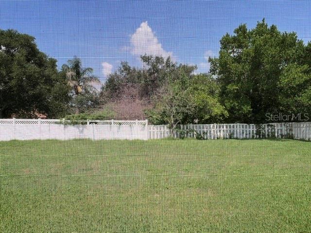 A grassy backyard features a white lattice-topped fence and mature trees under a blue sky — 1206 BRENTWOOD DRIVE, CLERMONT, FL