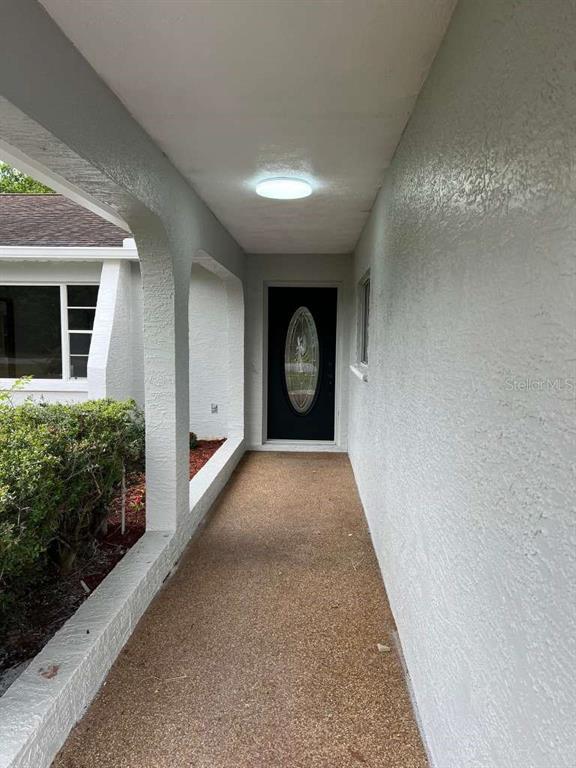 A covered entryway features a textured concrete walkway, arched pillars, and a dark front door — 6206 DORSET ROAD, SPRING HILL, FL