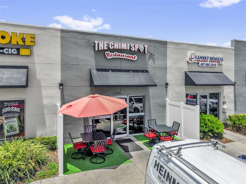 The exterior of a commercial building features a restaurant entrance with outdoor patio seating — 3900 S GOLDEN ROAD UNIT 136, ORLANDO, FL