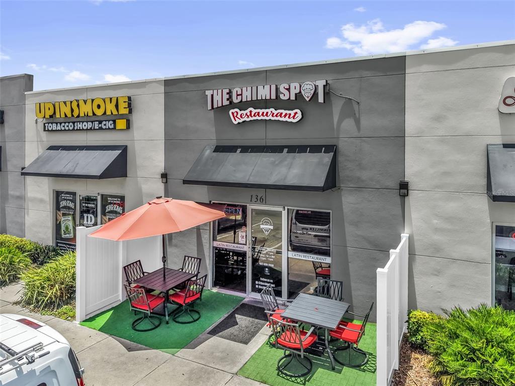 An exterior view of a restaurant storefront with outdoor patio seating and a tobacco shop — 3900 S GOLDEN ROAD UNIT 136, ORLANDO, FL