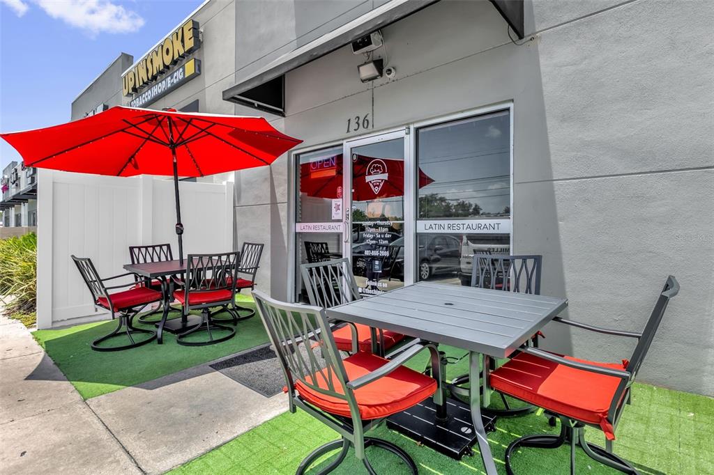 A Latin restaurant storefront features outdoor seating with two tables and red-cushioned chairs under umbrellas — 3900 S GOLDEN ROAD UNIT 136, ORLANDO, FL
