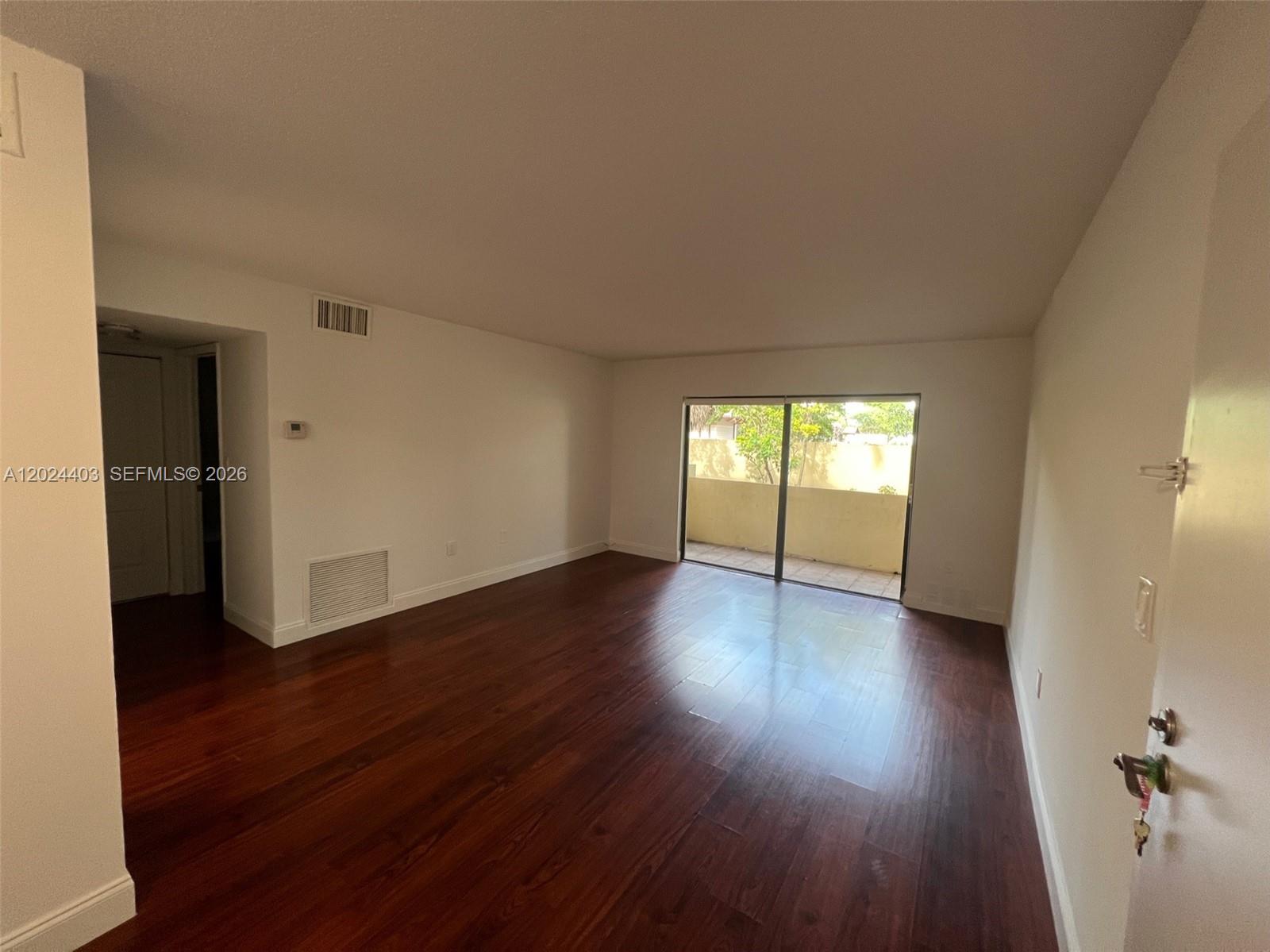 An empty living room features dark wood flooring, white walls, and a sliding glass balcony door — 10415 N Kendall Dr # B113, Miami FL 33176, MIAMI, FL