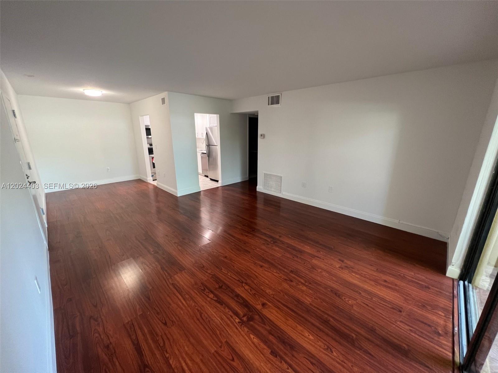 An empty living room features dark wood-look flooring, white walls, and an adjacent kitchen — 10415 N Kendall Dr # B113, Miami FL 33176, MIAMI, FL