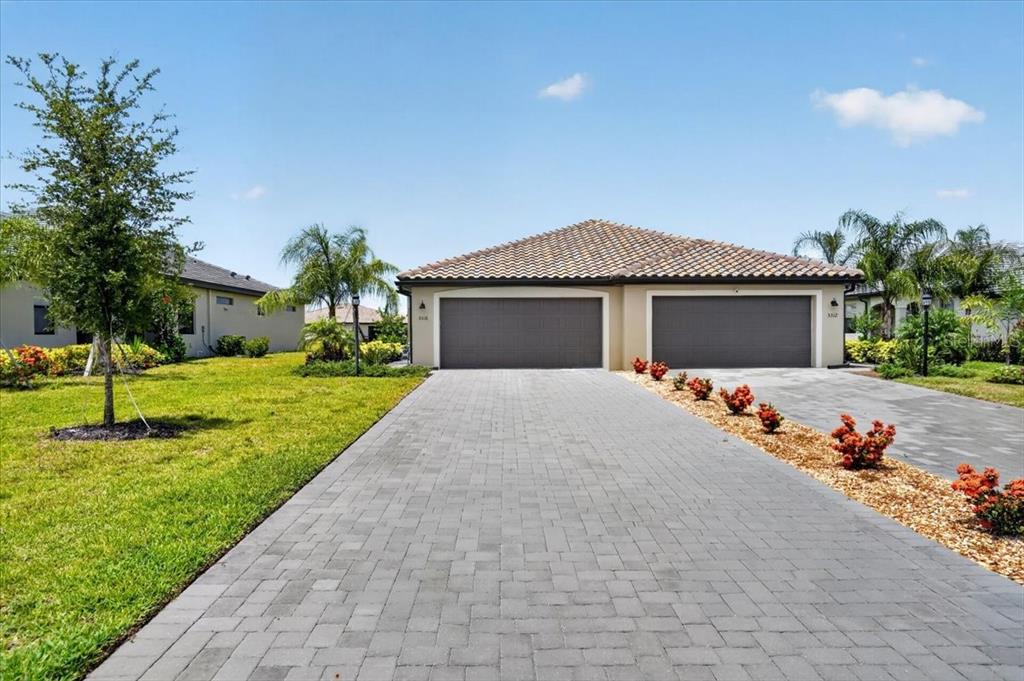 A single-story house with a two-car garage and a paved driveway under a blue sky — 5316 CRYSTAL HARBOR COVE, BRADENTON, FL