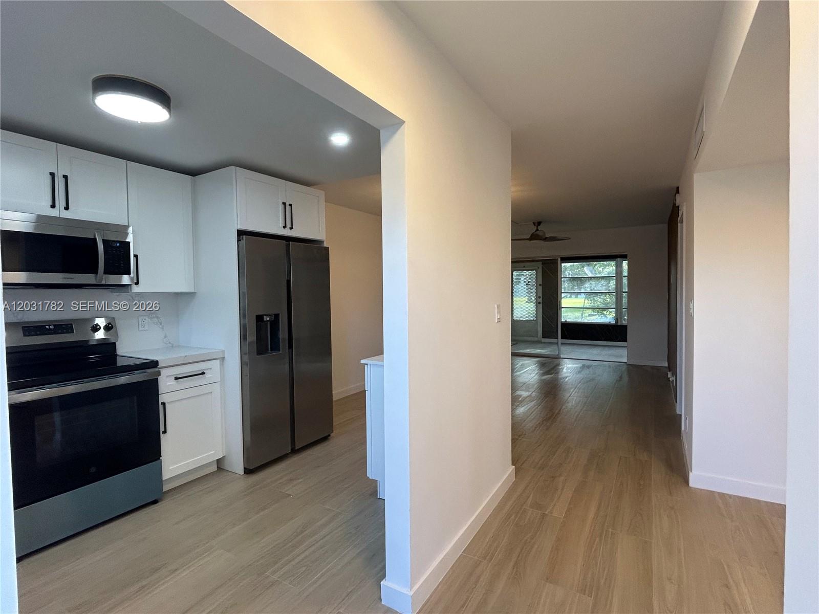 A kitchen with white cabinets and stainless steel appliances opens into a living area — 609 S State Road 7 # 1E, Margate FL 33068, MARGATE, FL