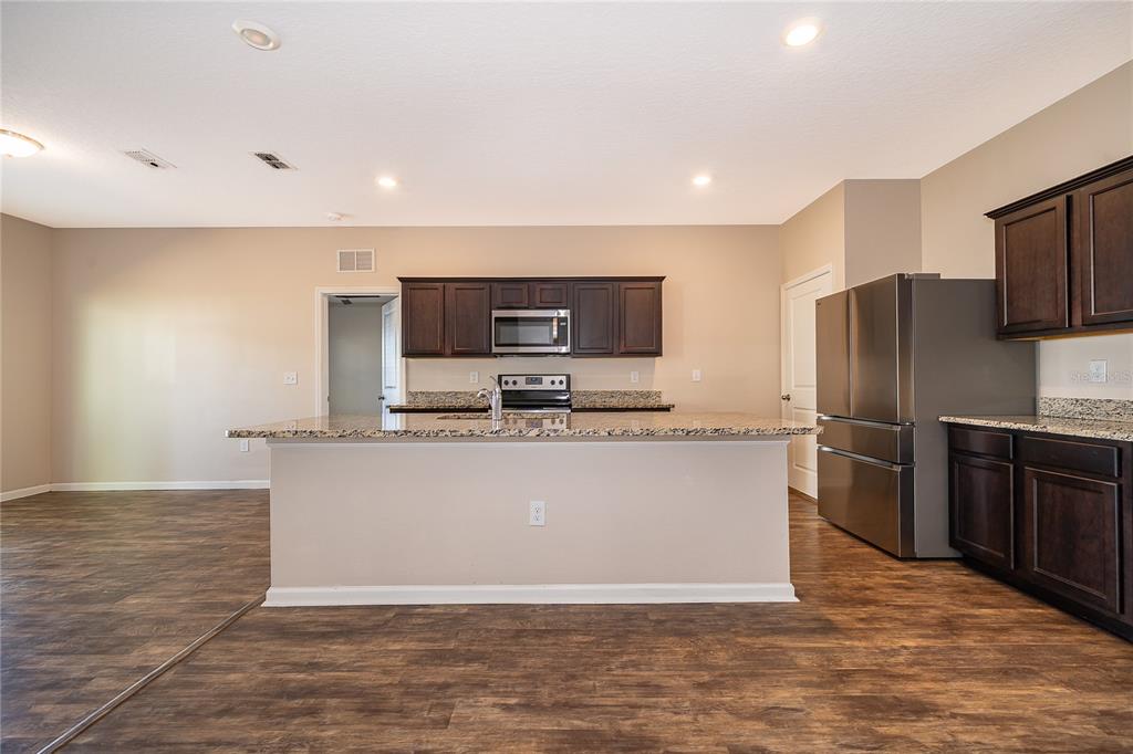 A kitchen features dark wood cabinets, granite countertops, stainless steel appliances, and wood-look flooring — 15824 SURFBIRD COURT, MASCOTTE, FL