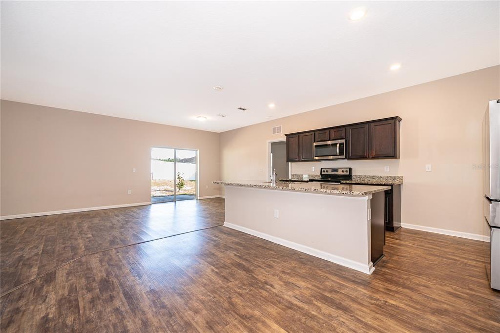 An open-concept kitchen with dark wood cabinets and a granite island overlooks a living area — 15824 SURFBIRD COURT, MASCOTTE, FL