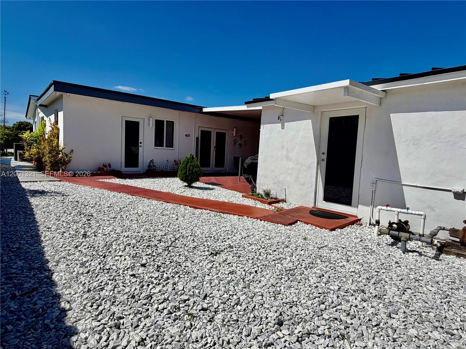 A white house exterior features a gravel yard, red concrete paths, and multiple entry doors — 11511 SW 180th St, Miami FL 33157, MIAMI, FL
