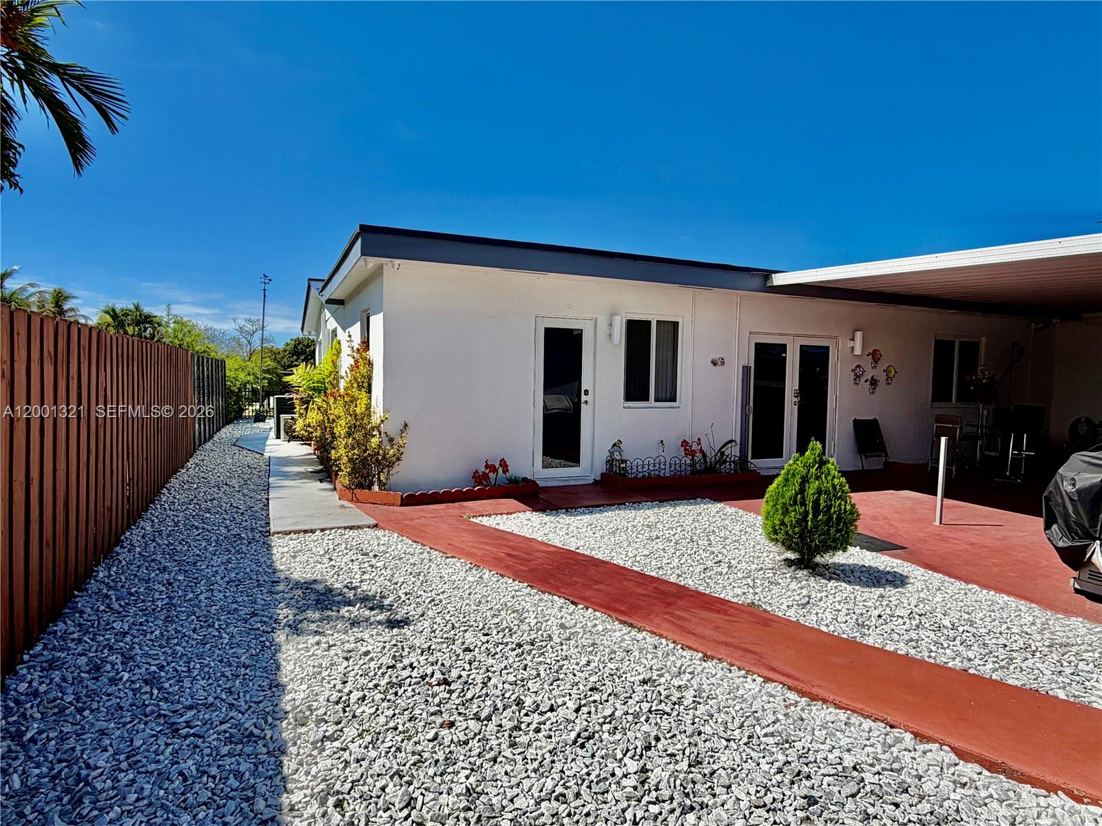 The exterior of a white house features a gravel yard, a red path, and a carport — 11511 SW 180th St, Miami FL 33157, MIAMI, FL