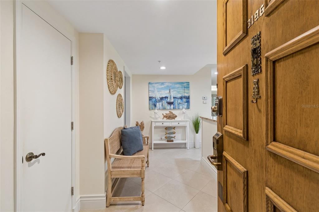 A wooden front door opens into a coastal-themed entryway with a bench and console table — 36750 US HIGHWAY 19 UNIT 21102, PALM HARBOR, FL