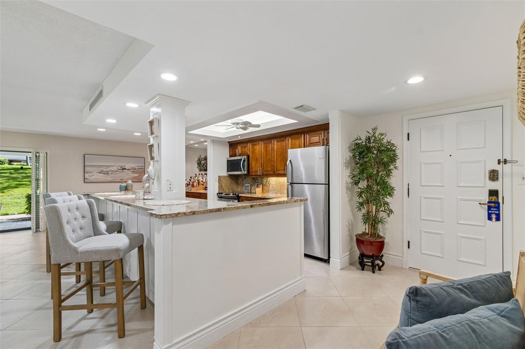 A kitchen with wooden cabinets and granite countertops overlooks a living area with bar seating — 36750 US HIGHWAY 19 UNIT 21102, PALM HARBOR, FL