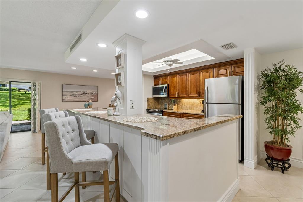 A kitchen features a granite-topped breakfast bar, wooden cabinetry, and light-colored tile flooring — 36750 US HIGHWAY 19 UNIT 21102, PALM HARBOR, FL